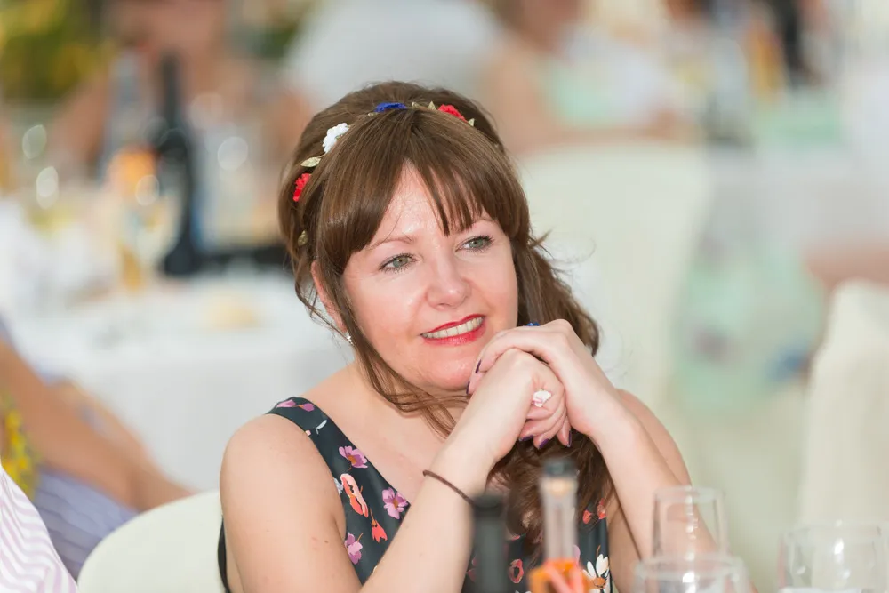 Smiling woman with brown hair and floral headband sitting at a table with folded hands.