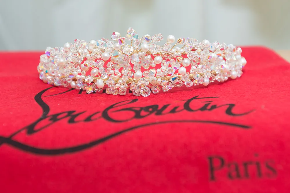 Delicate crystal and pearl embellished crown placed on a red fabric with 'Louboutin Paris' text.
