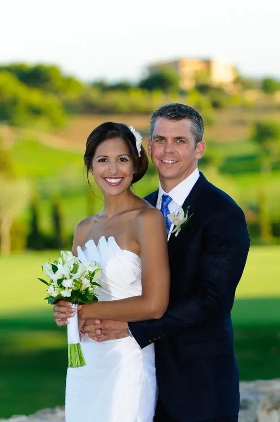 Bride and groom smiling and embracing outdoors with the bride holding a white flower bouquet.