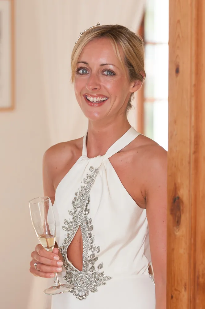 Smiling bride in a white embellished halter dress holding a champagne glass.