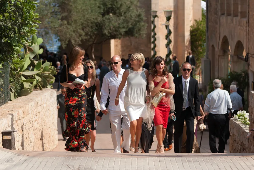 Group of people dressed in formal attire walking up stone steps outdoors on a sunny day.