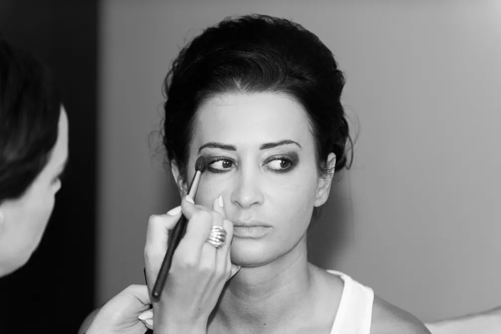Woman having eyeshadow applied with a brush by another person in a black and white close-up shot.