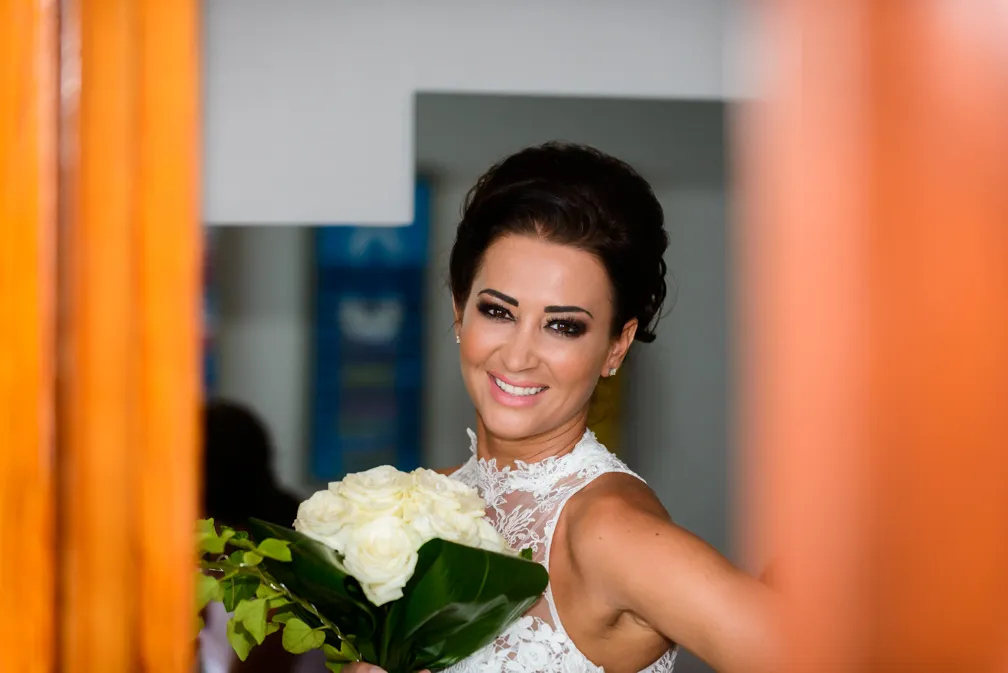 Smiling bride wearing a lace wedding dress holding a bouquet of white roses.