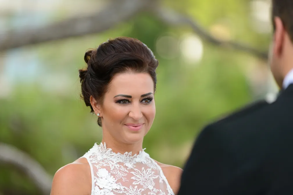 Bride with an elegant updo wearing a white lace wedding dress, smiling and looking at the groom.