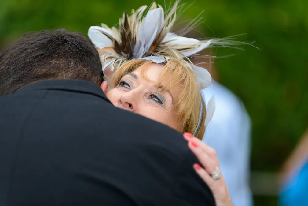 Woman with a decorative feather headpiece smiling and hugging a man in a black suit.