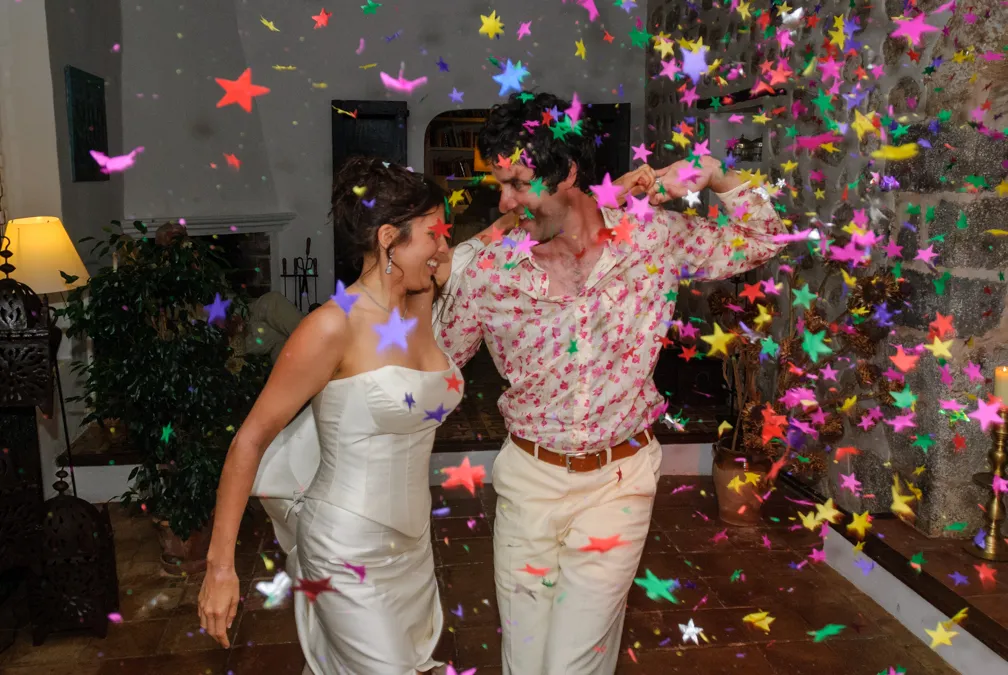 Bride and groom dancing indoors surrounded by colorful star-shaped confetti.