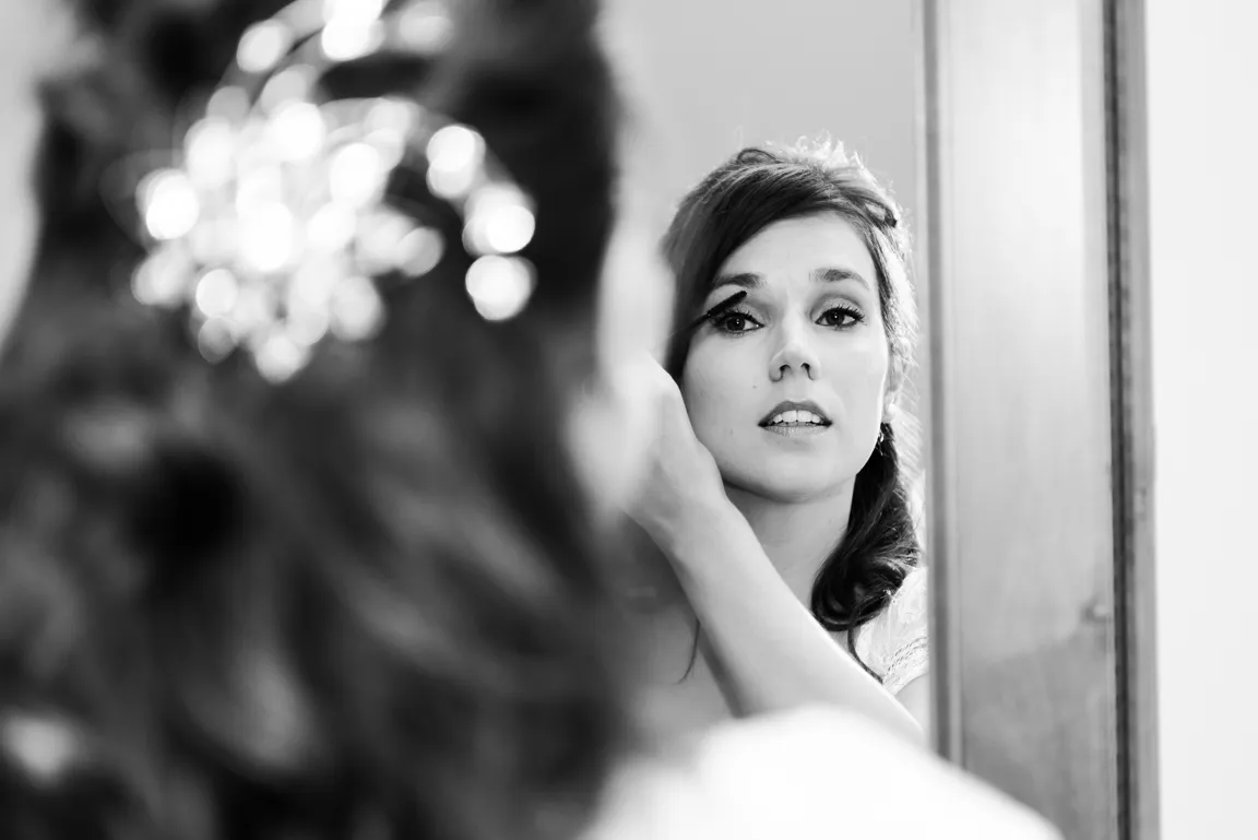 Black and white photo of a woman applying mascara while looking into a mirror.
