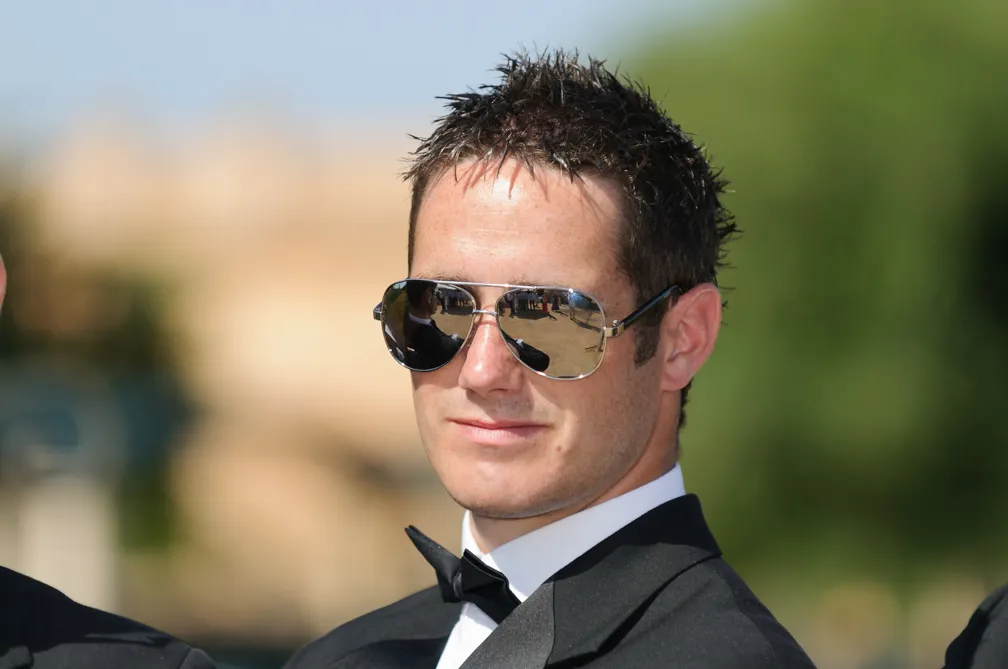 Man wearing dark suit, bow tie, and reflective sunglasses outdoors.