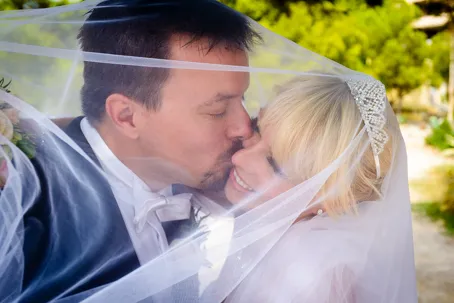 Bride and groom sharing a kiss under a sheer wedding veil outdoors.
