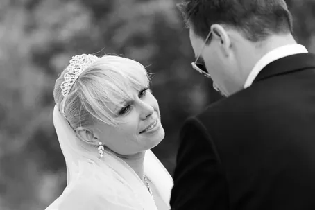 Bride smiling up at groom during an outdoor wedding ceremony in black and white.