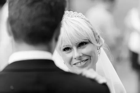 Bride with a tiara smiling warmly at groom during wedding ceremony.