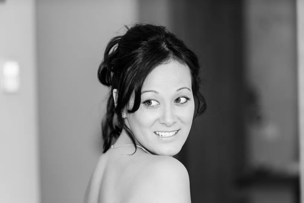 Black and white portrait of a woman with dark hair tied back, looking over her shoulder and smiling.