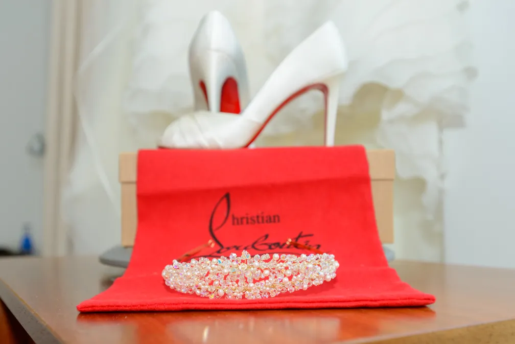 Pearl and crystal bridal headband on a red Christian Louboutin dust bag with white high-heeled shoes and a beige box in the background.
