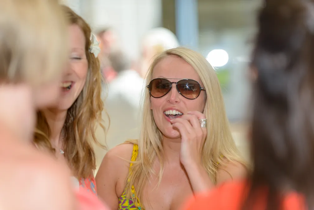 Smiling blonde woman wearing sunglasses and a colorful dress in a social gathering.