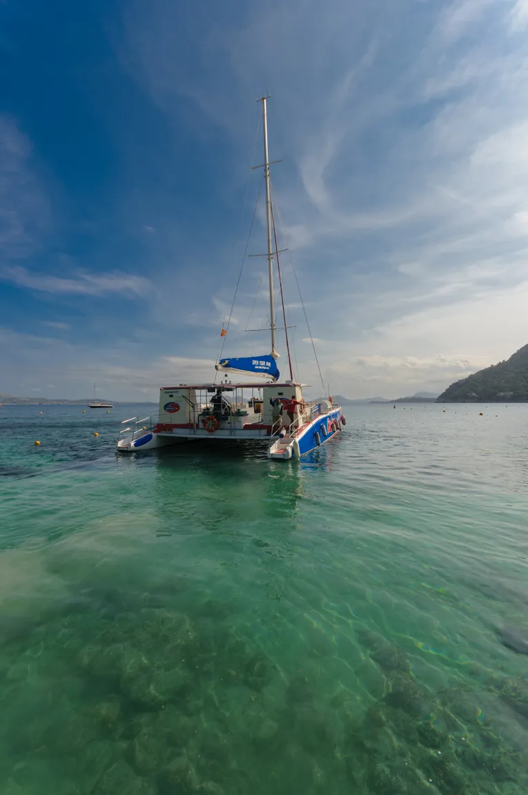 Catamaran sailboat anchored on clear turquoise water under a partly cloudy sky.
