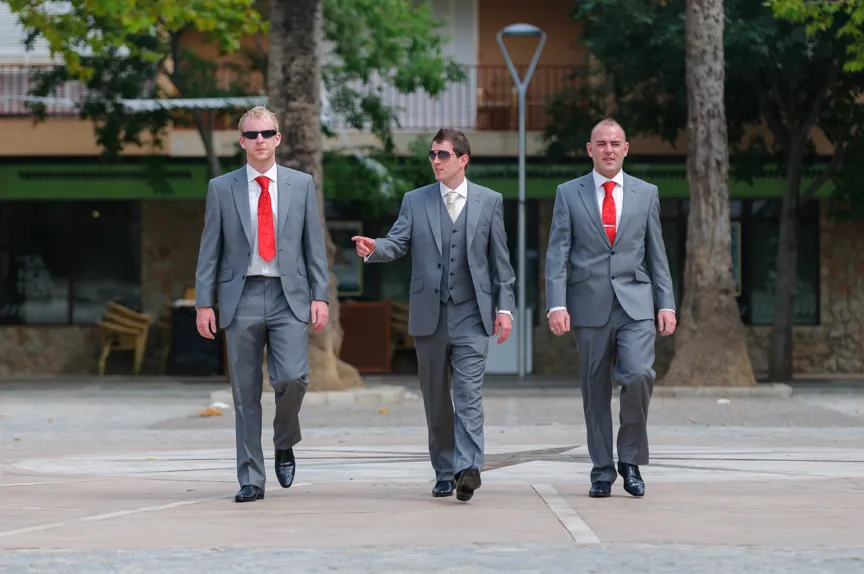 Three men in gray suits walking outdoors with two men wearing red ties and one in a beige tie.