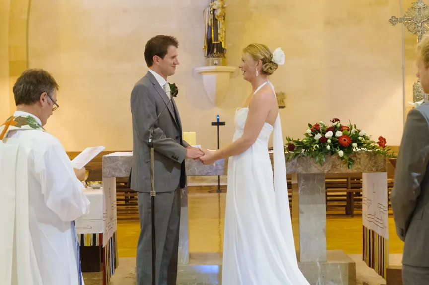 Bride and groom holding hands facing each other during wedding ceremony in church.