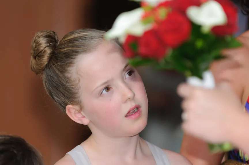 Young girl with hair in a bun looking attentively at a bouquet of red and white flowers.