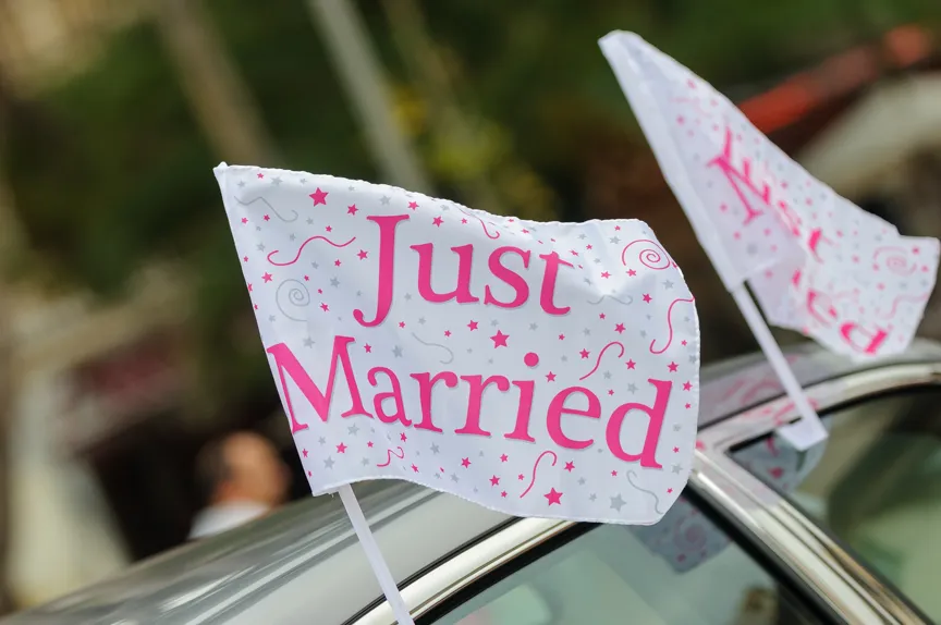 Two white flags with pink 'Just Married' text and decorative stars attached to a car roof.