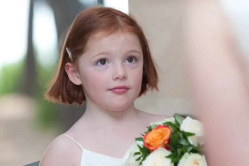 Young girl with short red hair looking up while holding a bouquet of white and orange roses.