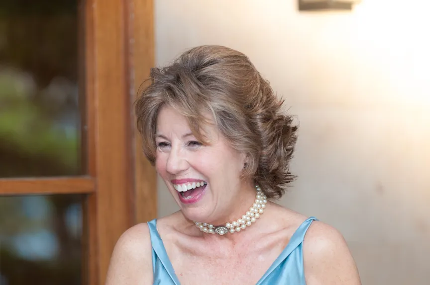 Smiling middle-aged woman with short wavy hair wearing a blue satin dress and pearl necklace.