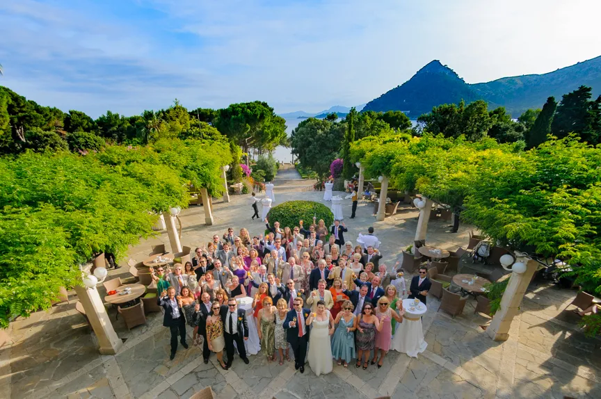 Large group of people posing for a photo at an outdoor event with green trees and a mountain in the background.
