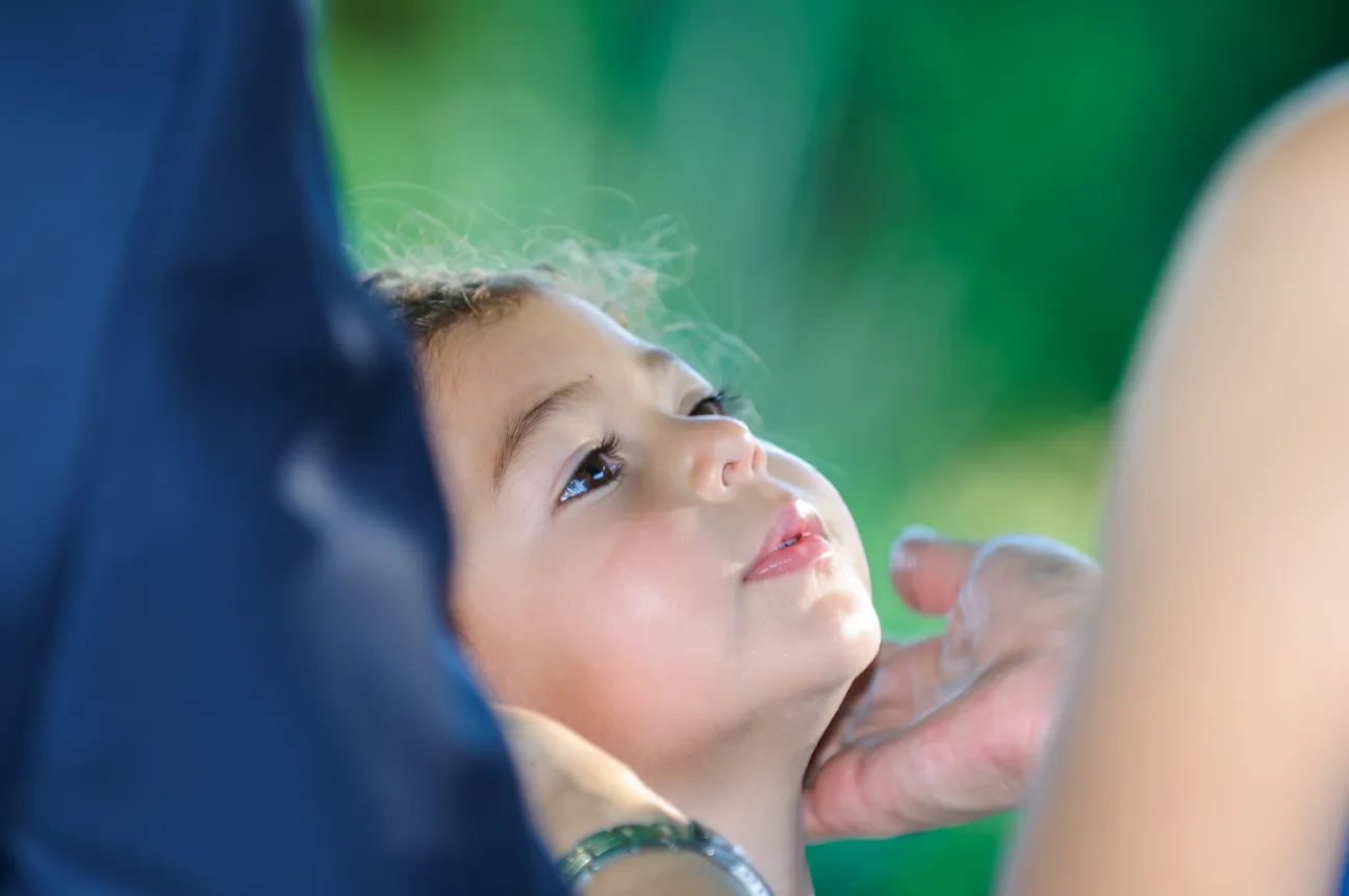 Close-up of a child looking upwards while an adult gently touches their neck.