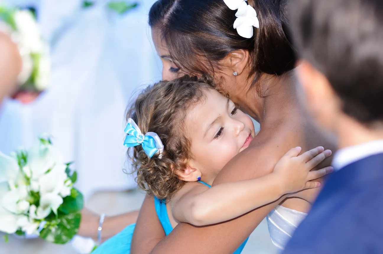 Young girl in blue dress hugging a woman with flowers in her hair at a formal event.