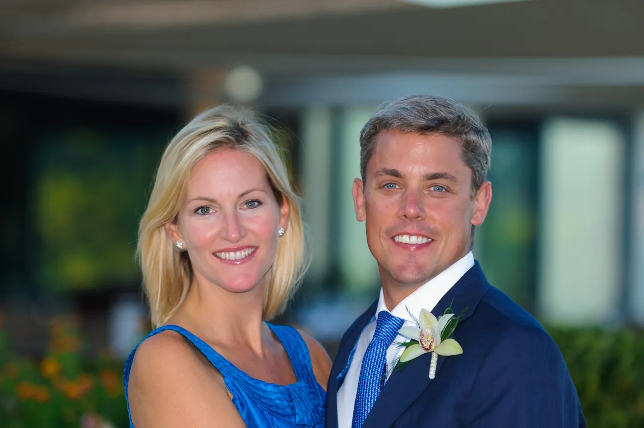 Smiling couple dressed in blue, with the man wearing a suit and boutonniere and the woman in a sleeveless dress.