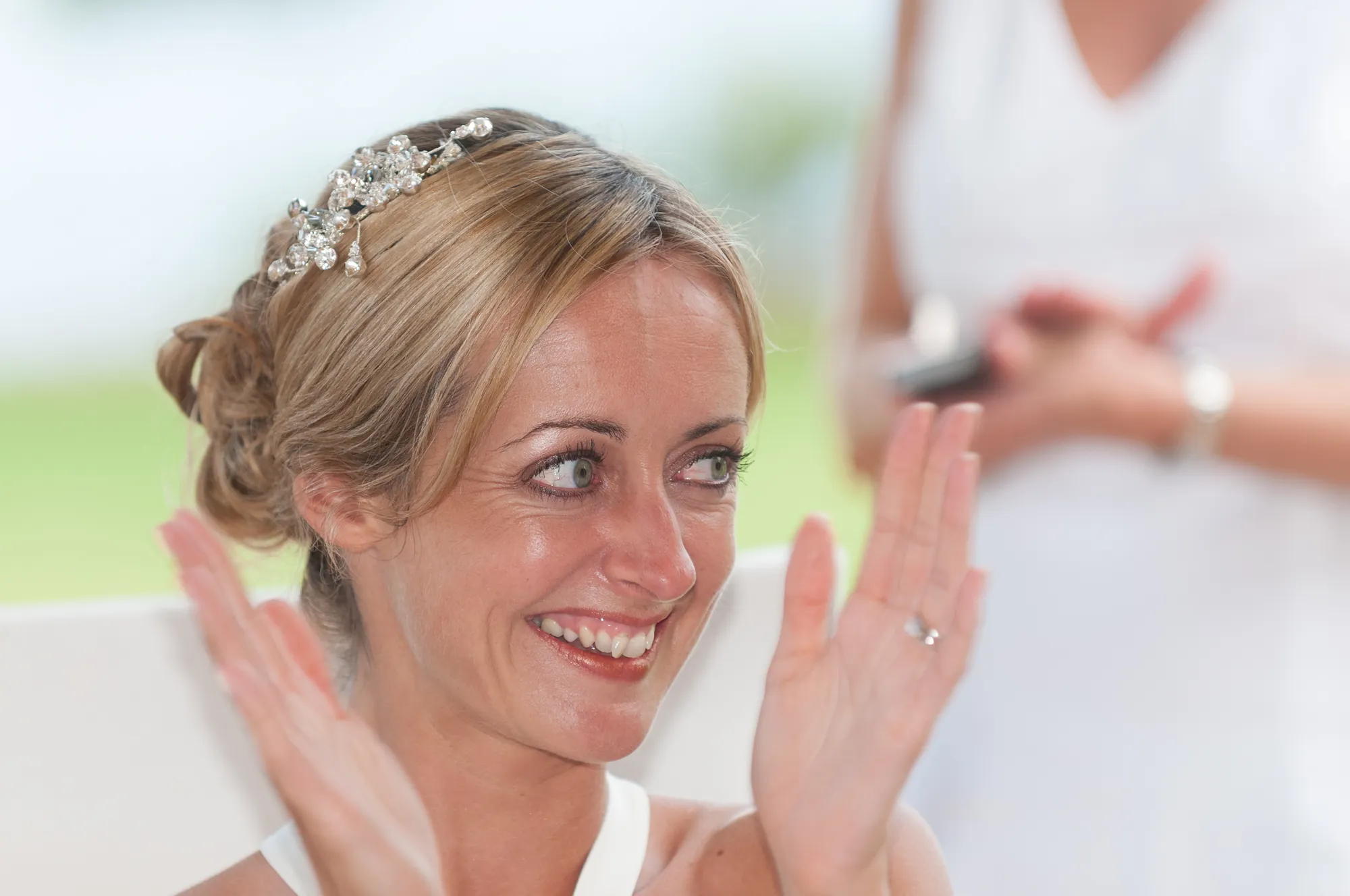 Smiling woman with blonde hair styled up and a decorative hair accessory, clapping her hands.
