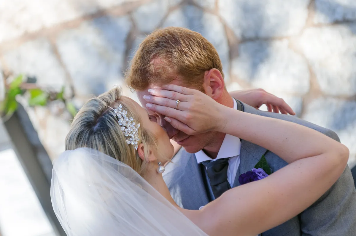 Bride with a jeweled hairpiece and veil covering groom's eyes with her hand during a wedding moment.