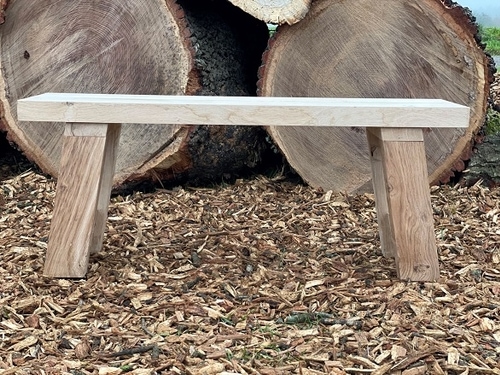 Eiken tuinbankje met twee boomstammen op de achtergrond op een bodem van zaagsel.