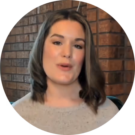 Young woman with shoulder-length brown hair speaking, with a brick wall background.