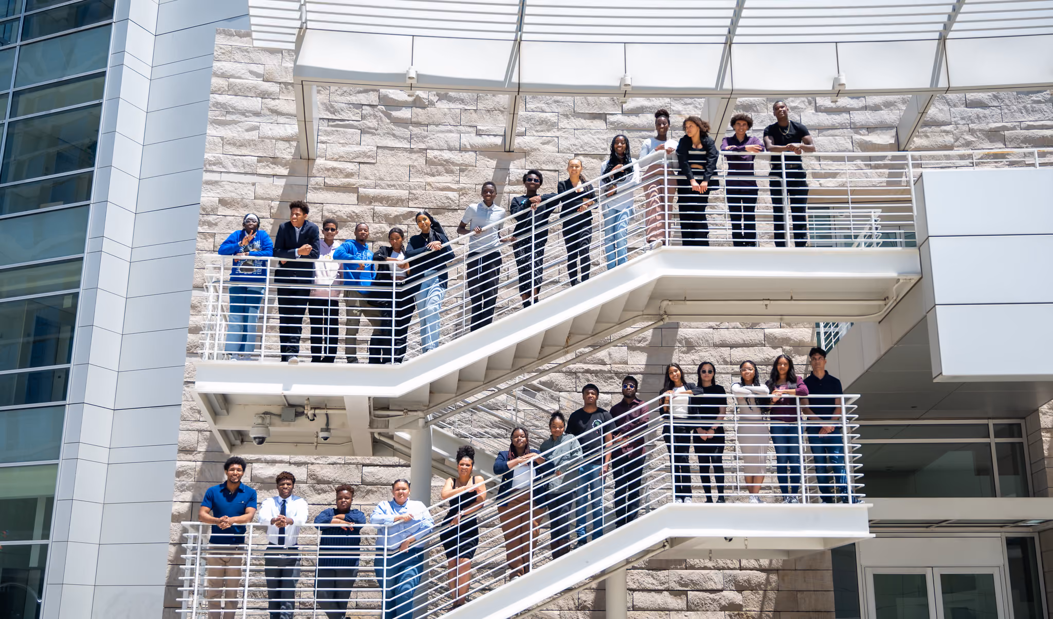 Participants stand along the white railings of an outdoor staircase at a modern building.