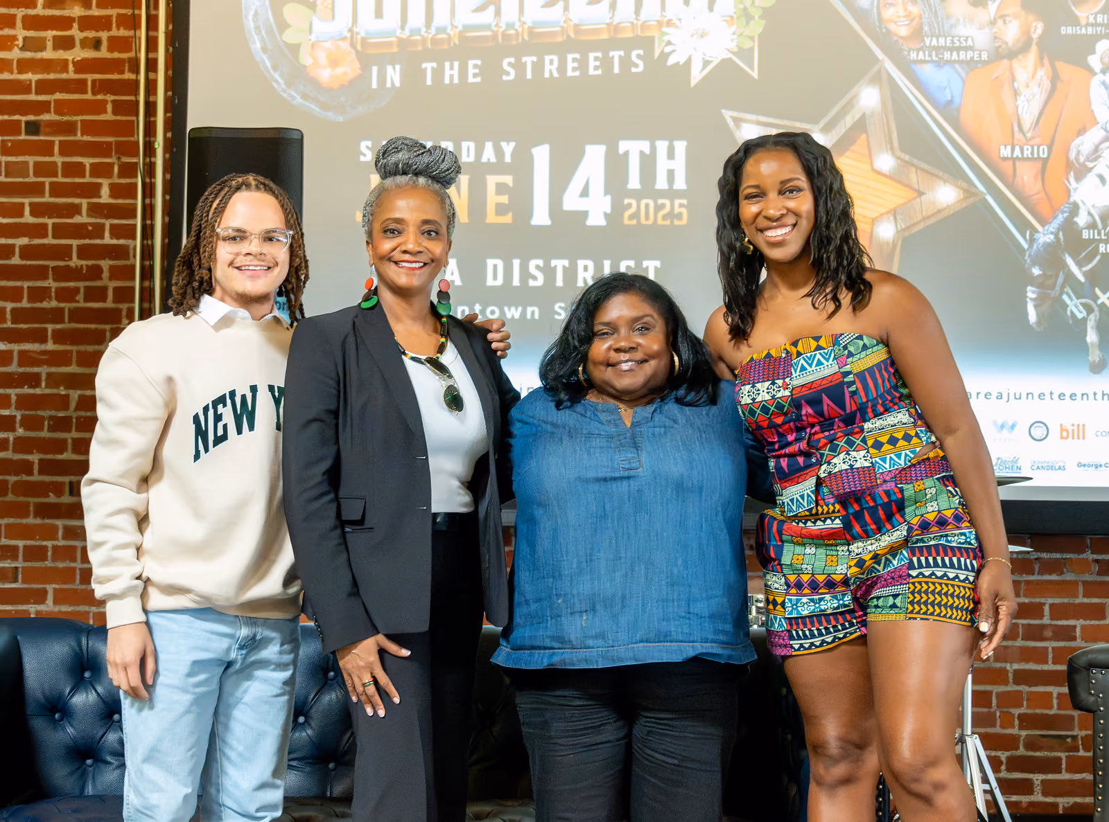 Four guests pose together in front of a projected Juneteenth festival poster inside a brick-walled venue