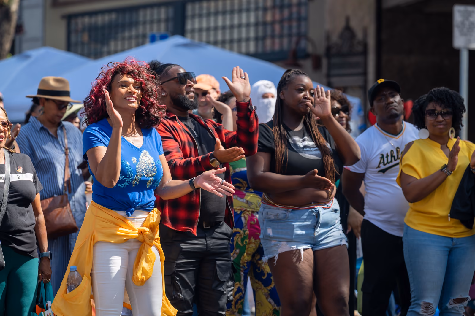 Festival attendees clap and raise their hands while watching a performance near vendor tents