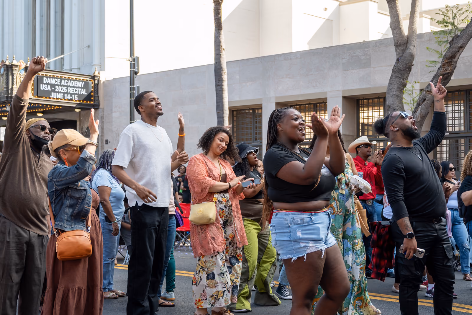 Festival attendees clap and raise their hands in the street near a theater marquee