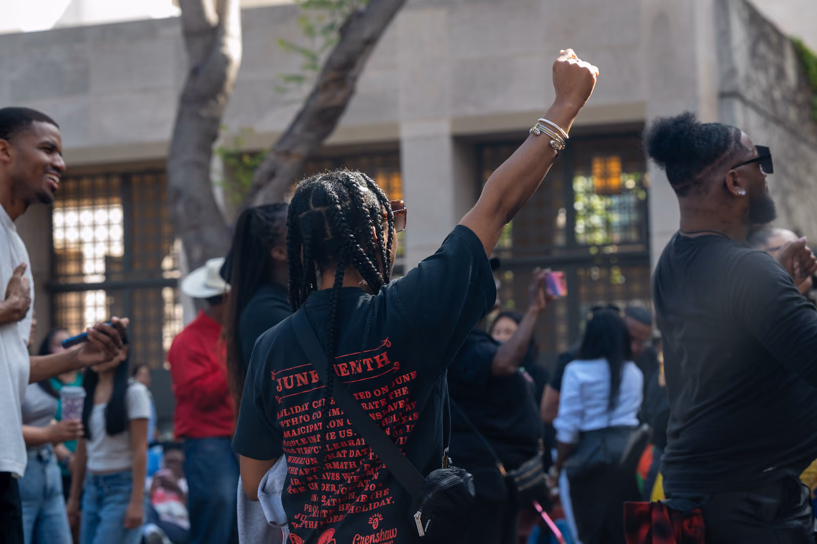 An attendee wearing a black Juneteenth shirt raises a fist while standing among the festival crowd