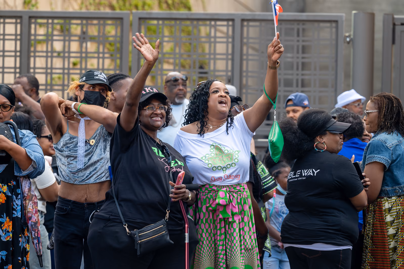 Two smiling attendees raise their arms, with one holding a small flag amid the outdoor festival crowd