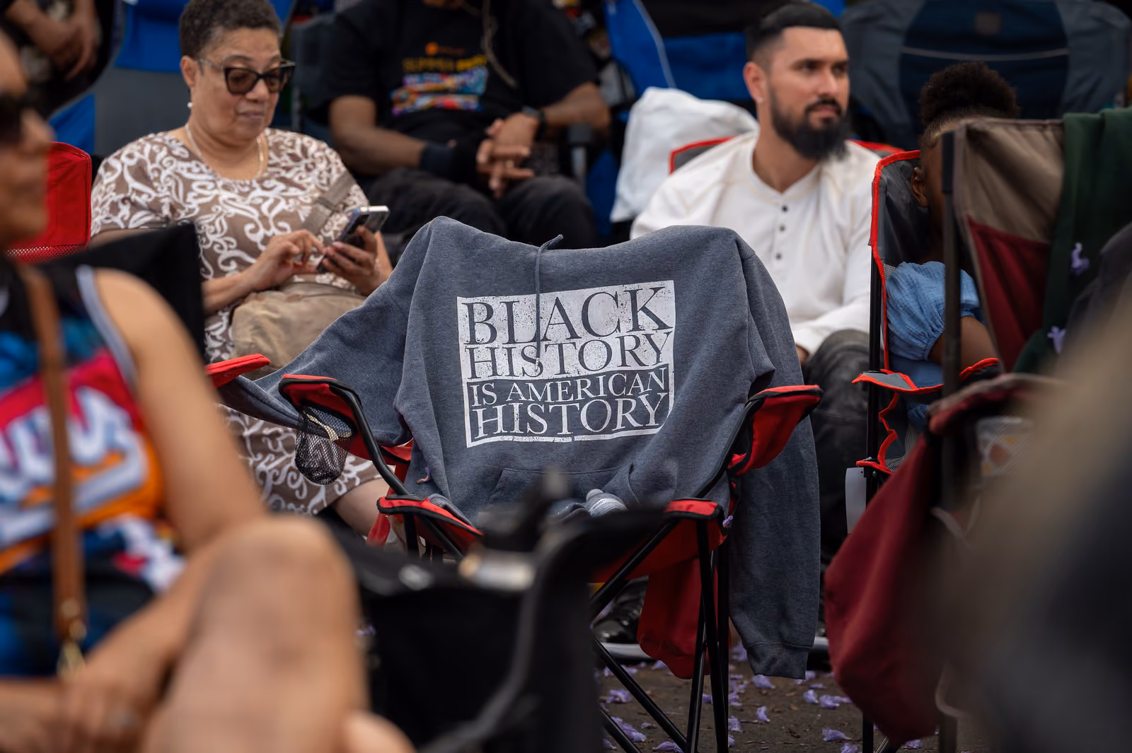 A gray hoodie reading “Black History Is American History” hangs over a folding chair among seated guests