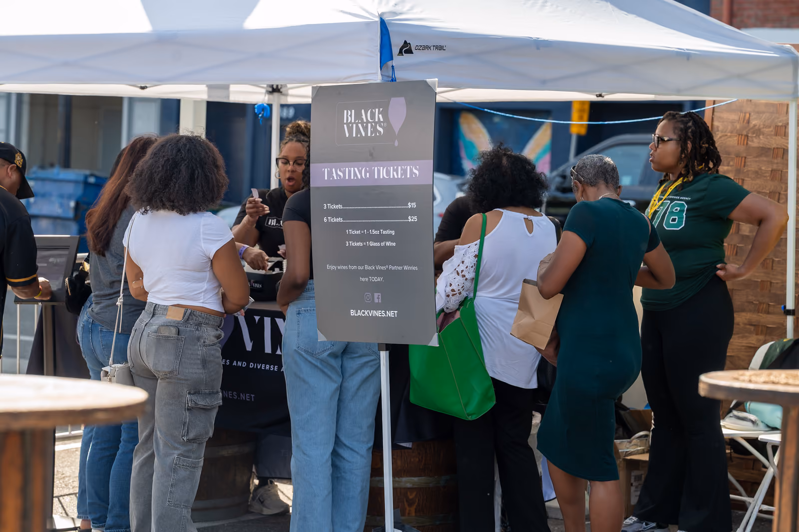 Festival visitors gather at a Black Vines wine booth beside a sign listing tasting ticket prices