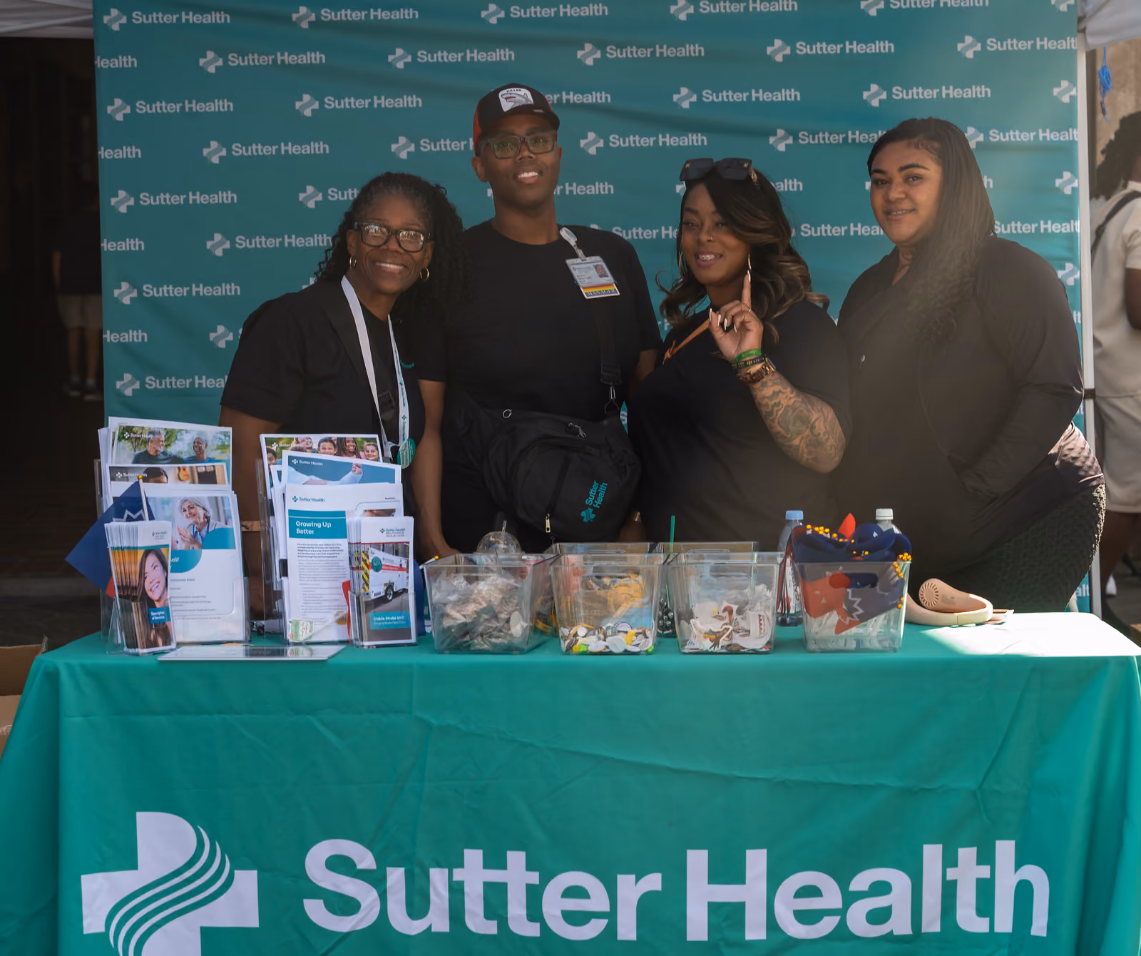 Four people pose behind a Sutter Health information table with brochures and giveaway bins