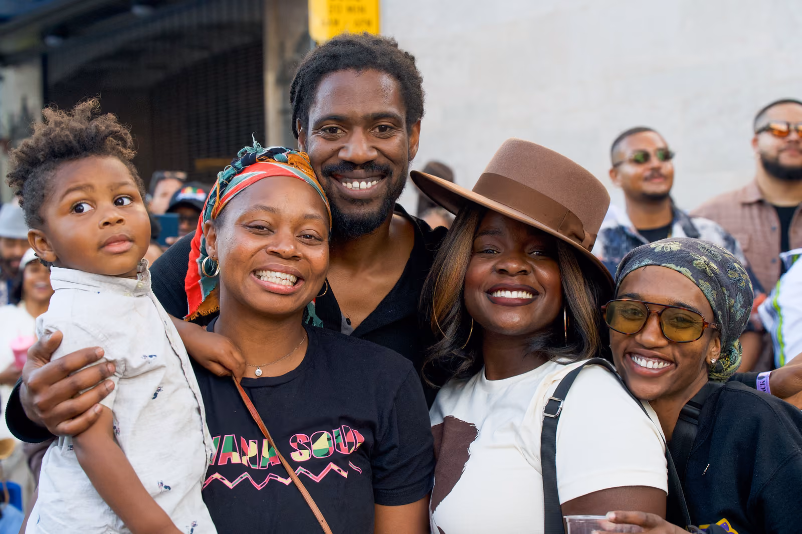 Four smiling adults and a small child pose together in the crowd, including a guest in a brown hat