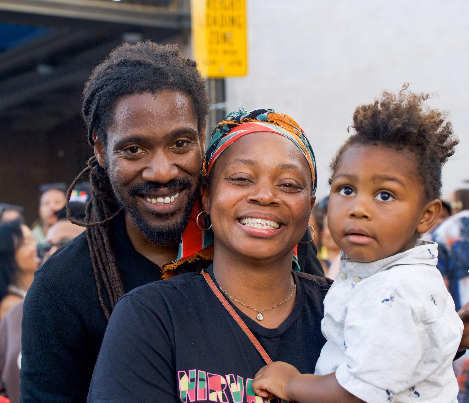 Two smiling adults pose closely with a small child in a white shirt amid the festival crowd