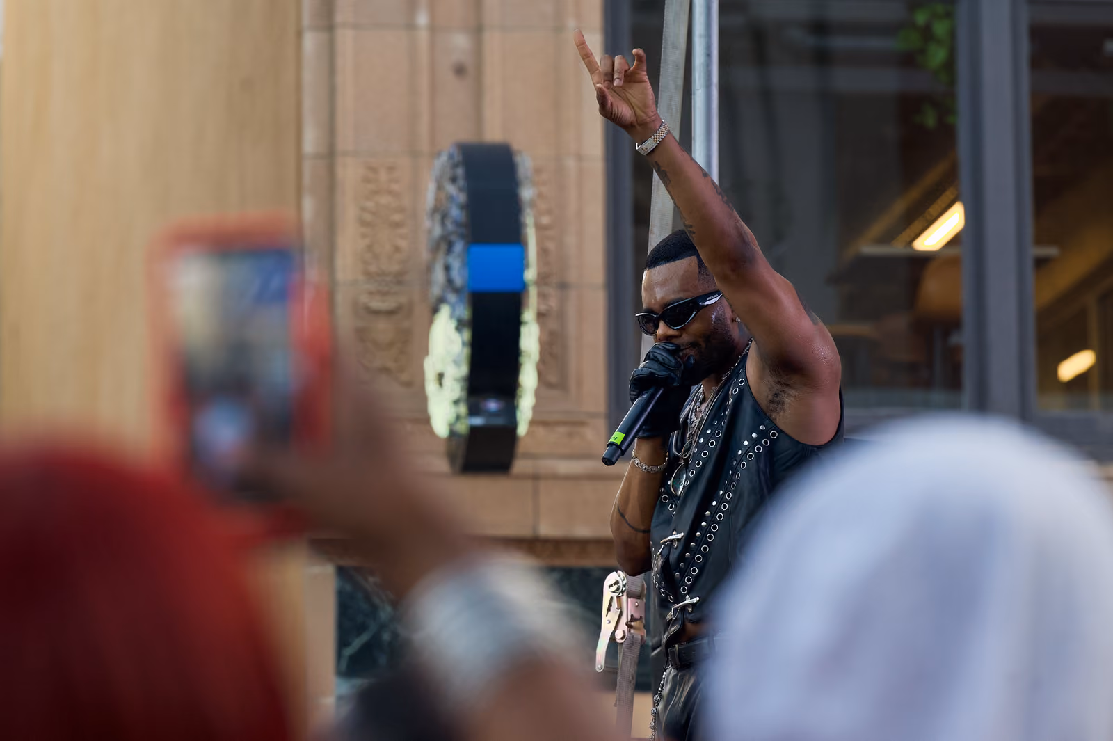 A singer raises one arm overhead while holding a microphone as audience members lift phones around him