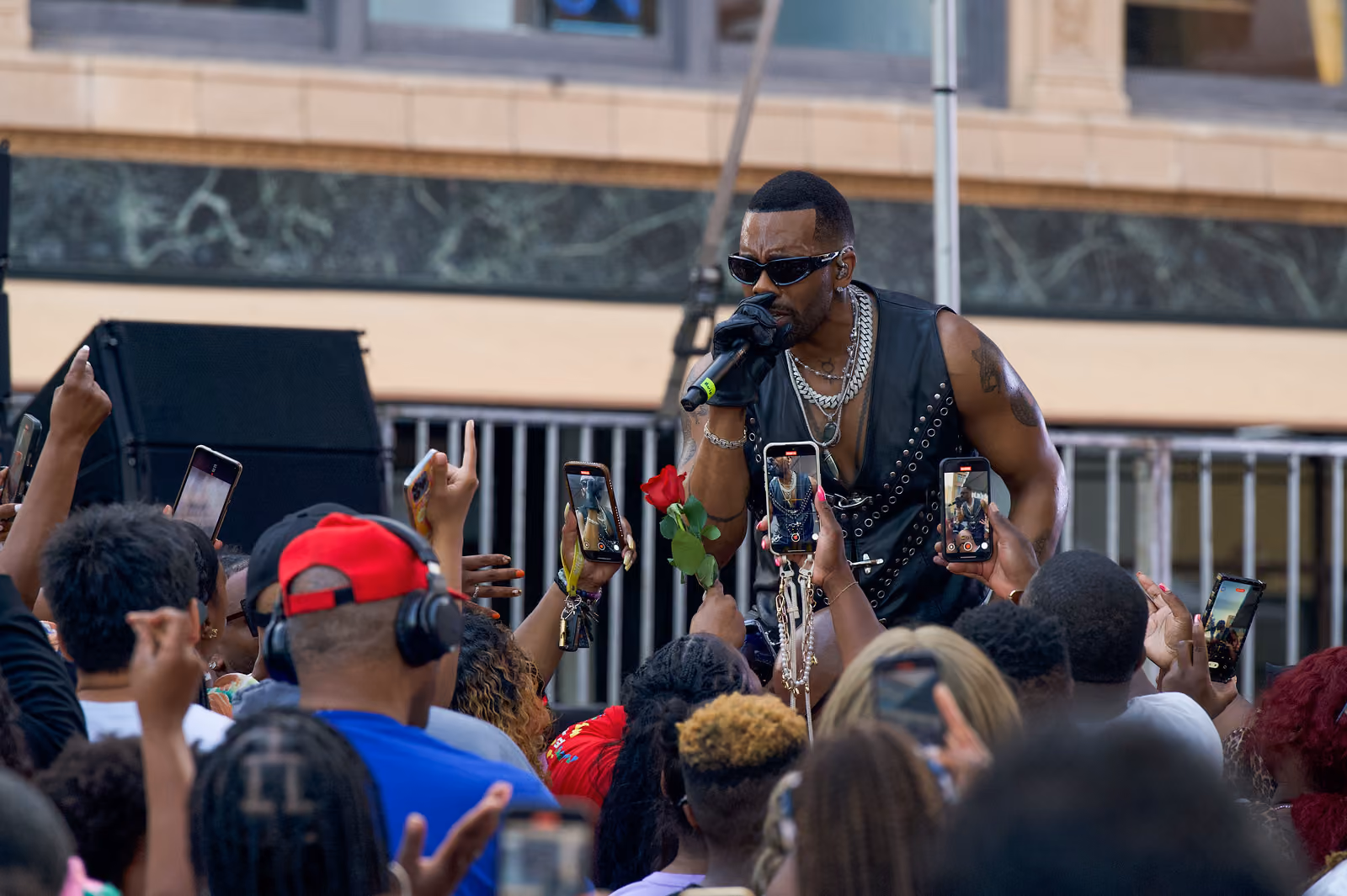 A singer leans toward a tightly packed crowd holding up phones and a red rose near the stage