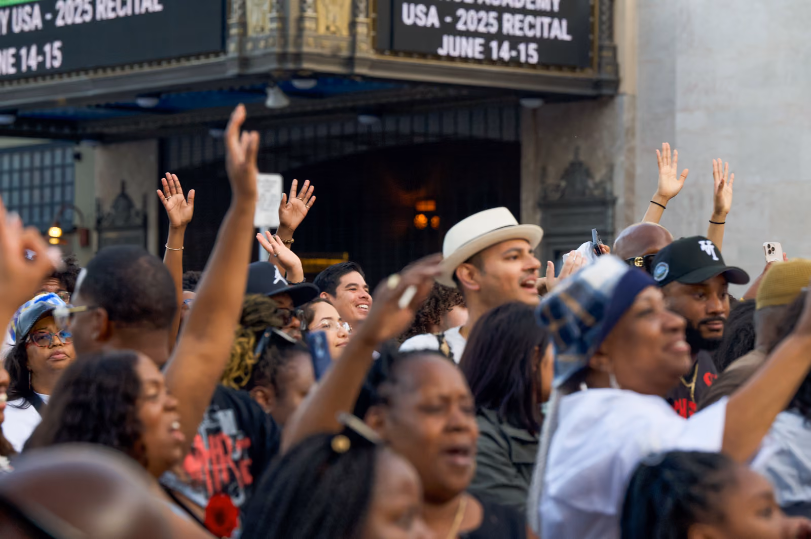 Festivalgoers raise their hands and sing along in a dense crowd beneath a theater marquee