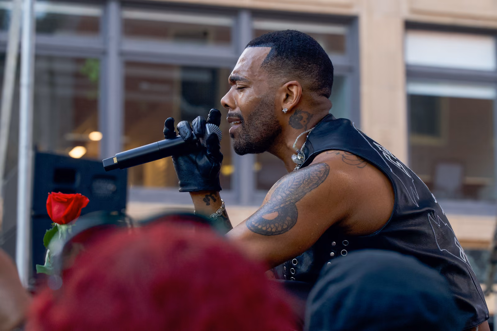A singer with an in-ear monitor sings in profile near the crowd, with a red rose raised beside him