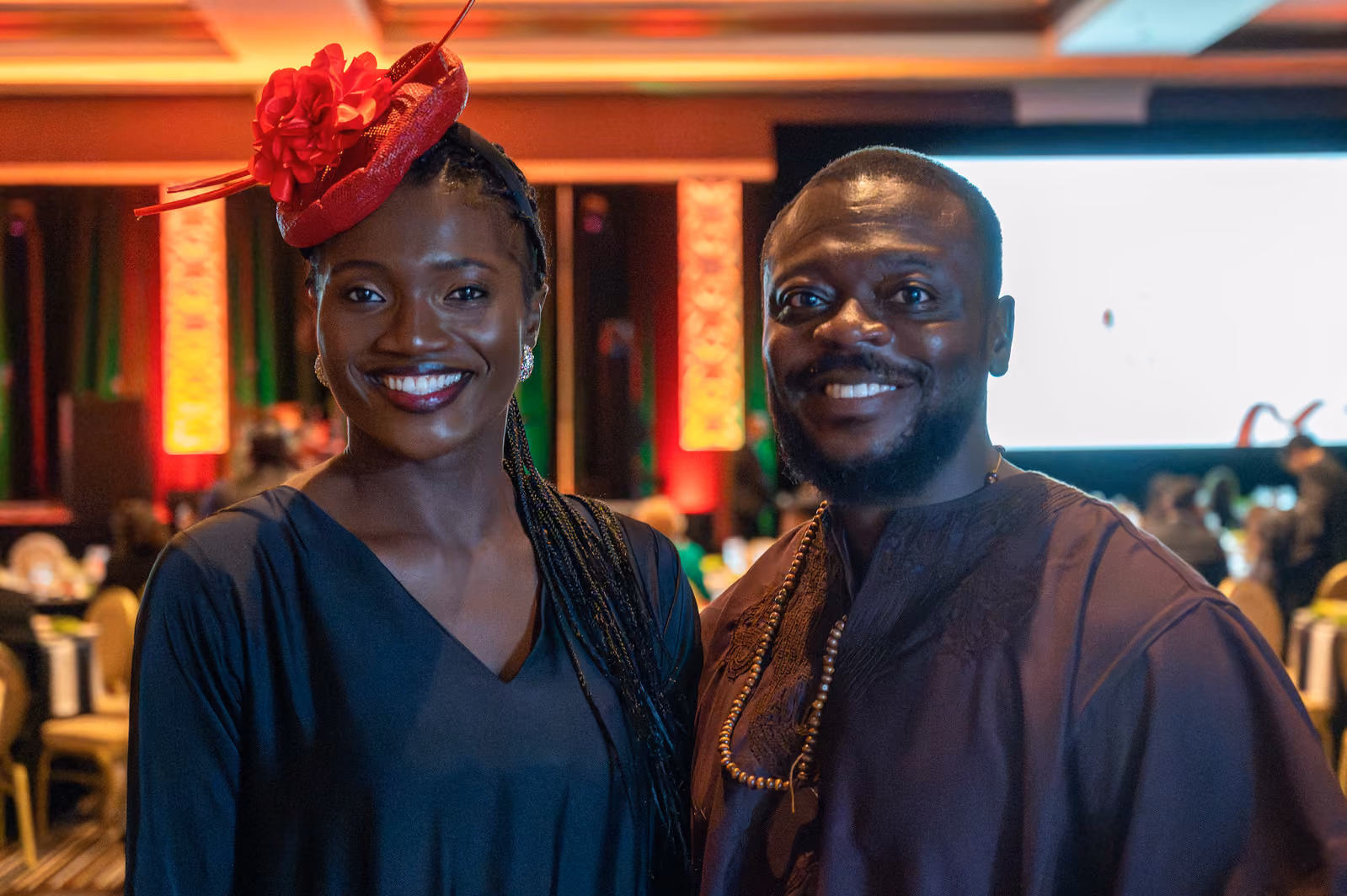 Two smiling guests, one wearing a red floral fascinator, pose together in the gala ballroom