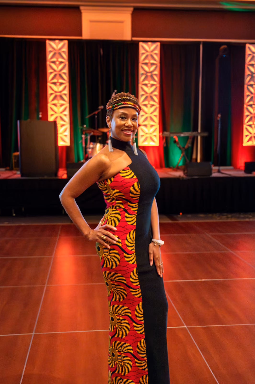 A guest in a black gown with a red and yellow patterned panel poses on the dance floor near the stage
